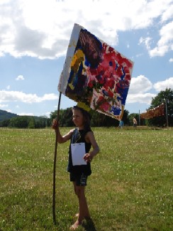 Ein Kind steht mit einer bunt bemalten Fahne auf einer Wiese